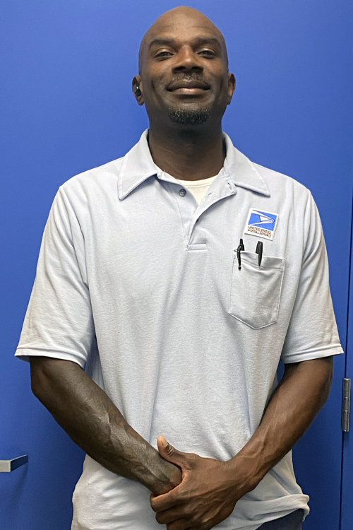 A uniformed USPS employee standing in front of a blue door