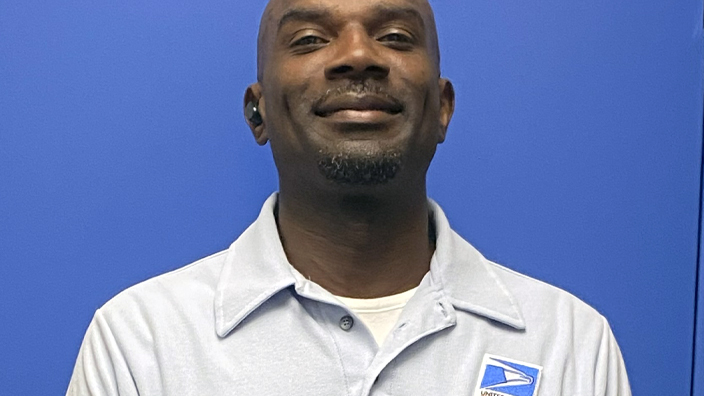 A uniformed USPS employee standing in front of a blue door