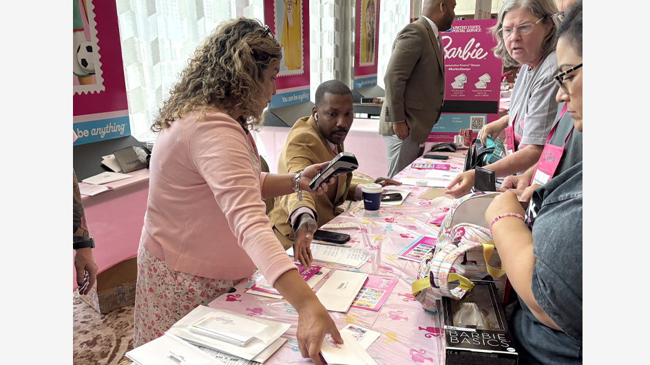 A standing woman and a seated man behind a table covered in pink.
