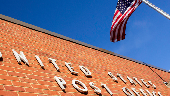 Brick exterior of a Post Office building with an American flag blowing in the wind out front