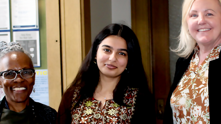 Three women standing on either side of a woman in the center who is holding a package
