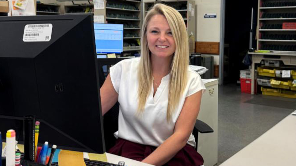 A woman with blonde hair and white top sits behind a desk