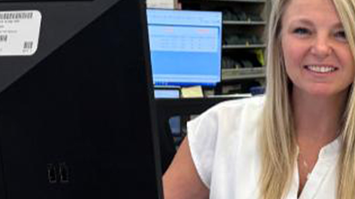 A woman with blonde hair and white top sits behind a desk