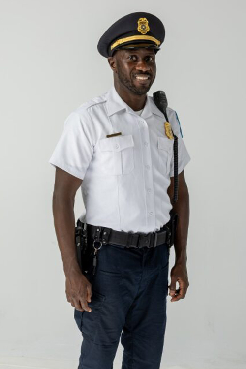 ALT TEXT: A man wearing a postal police uniform of a white button-down shirt, dark blue trousers and dark blue cap.