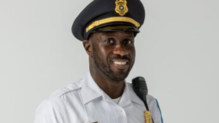 A man wearing a postal police uniform of a white button-down shirt, dark blue trousers and dark blue cap.