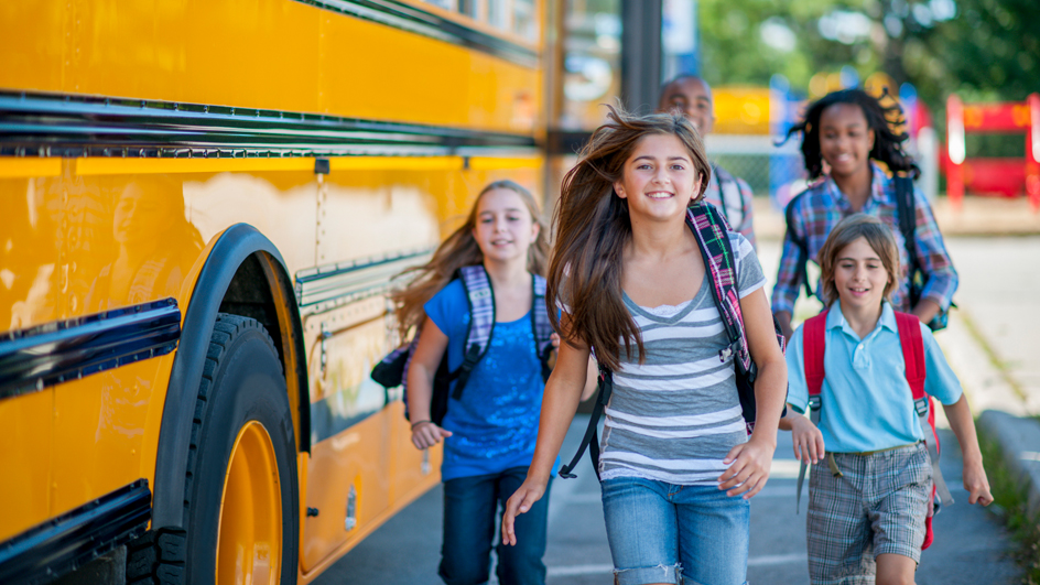 A group of elementary school-aged schoolchildren running next to a yellow school bus