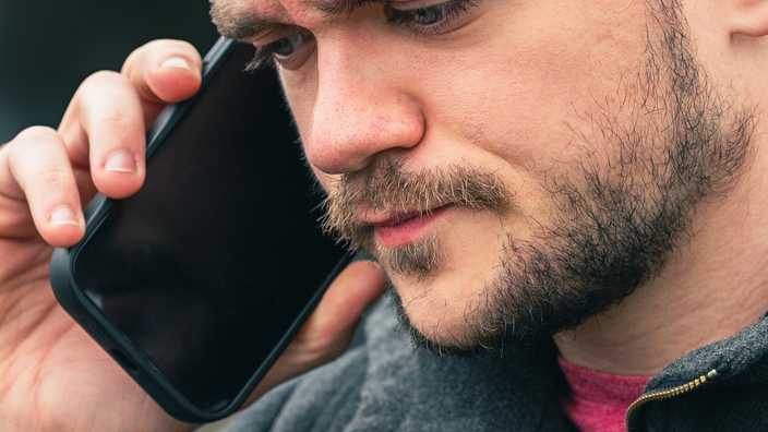 Man wearing a black coat and standing outdoors while holding a cellphone to his ear