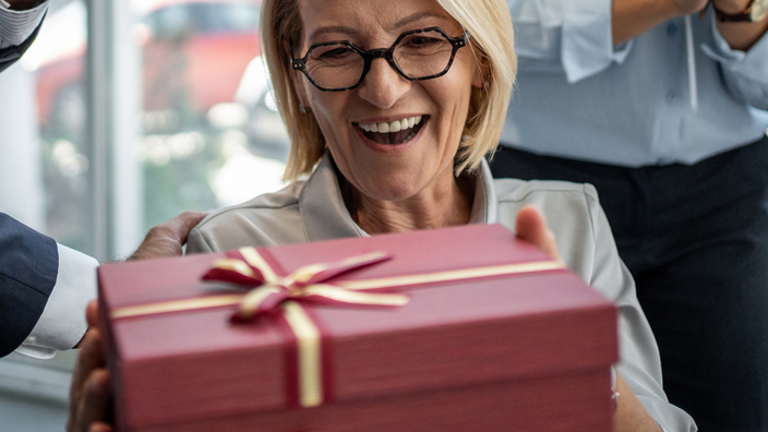 Group of co-workers surprising their colleague with a gift and flowers in the office
