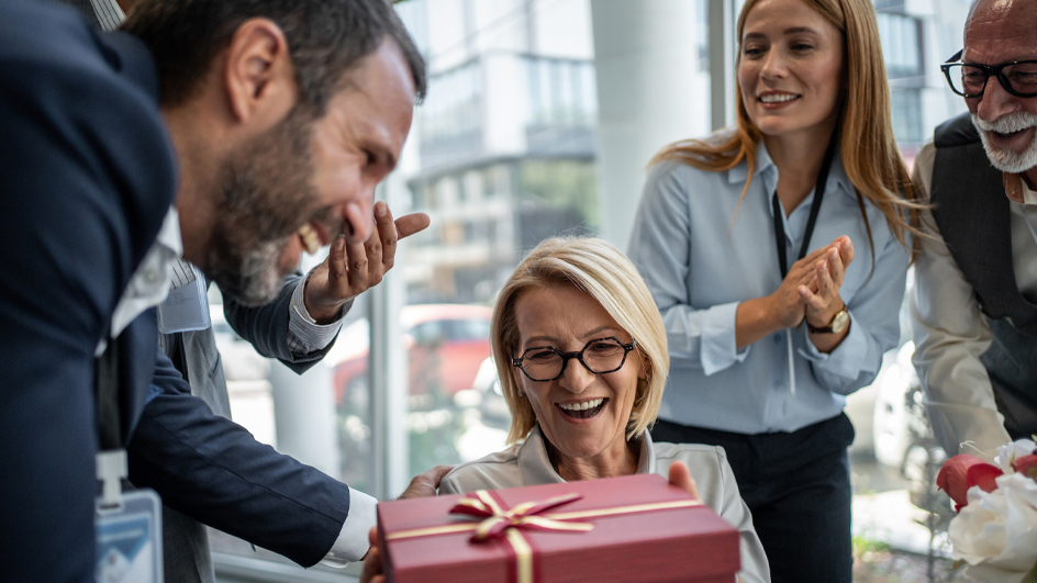 Group of co-workers surprising their colleague with a gift and flowers in the office
