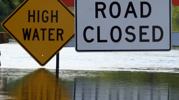 High flood waters and warning signs reading “High Water” and “Road Closed”