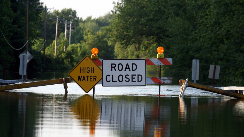 High flood waters and warning signs reading “High Water” and “Road Closed”