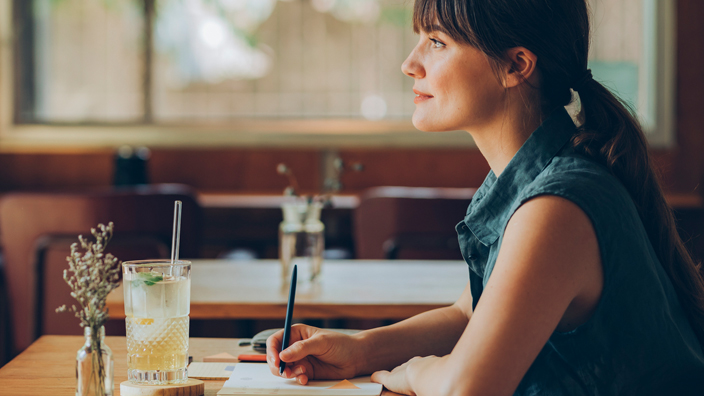 Profile of a woman sitting at a café table writing in a notebook
