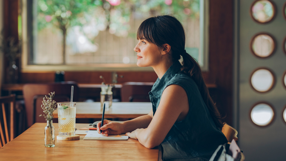 Profile of a woman sitting at a café table writing in a notebook
