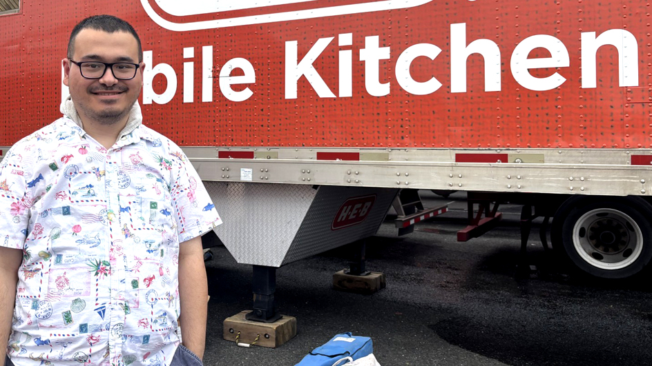Man in a patterned shirt standing in front of a red mobile kitchen trailer