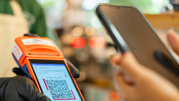 Person behind a cash register holding out a device showing a QR code
