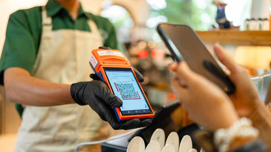 Person behind a cash register holding out a device showing a QR code
