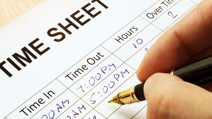 A hand holding a pen recording the hour on a time sheet