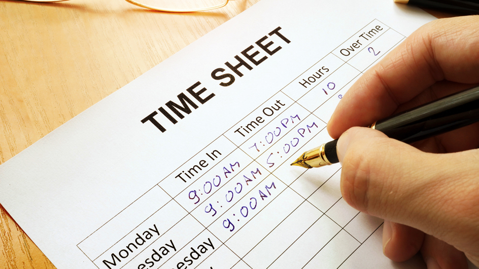 A hand holding a pen recording the hour on a time sheet