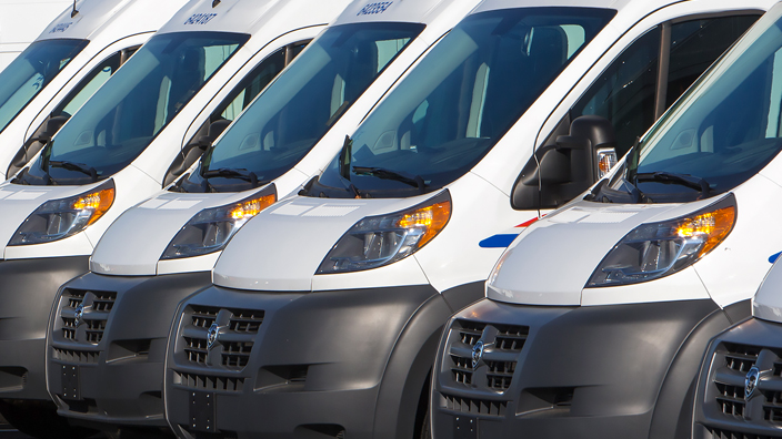 A row of USPS delivery vans in a parking lot
