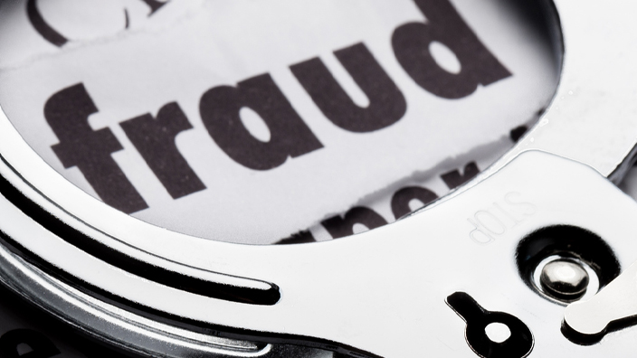 Handcuffs sitting on top of cut out words with the word “fraud” visible beneath the cuffs
