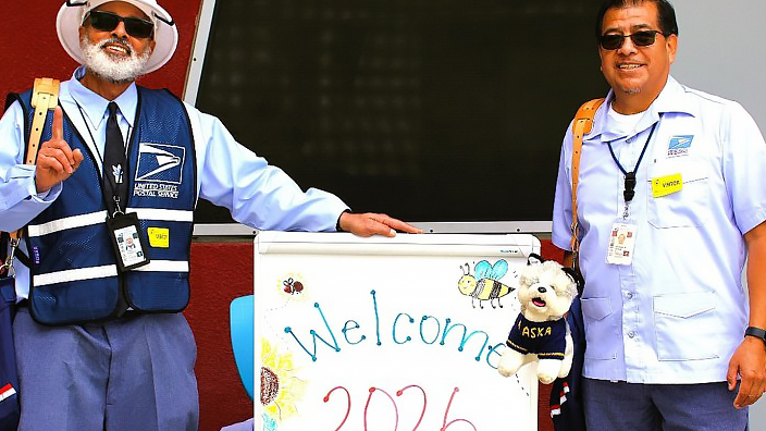 Two uniformed USPS employees standing next to a sign that reads “Welcome 2026 Career Day”