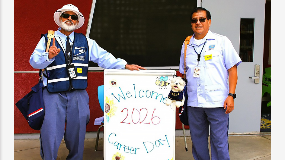 Two uniformed USPS employees standing next to a sign that reads “Welcome 2026 Career Day”