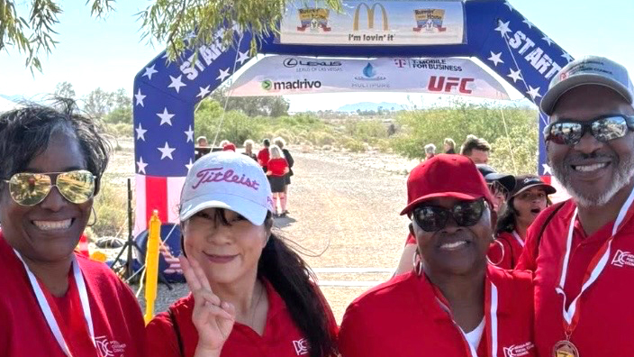 Four adults in red shirts standing side by side in front of a racecourse starting line
