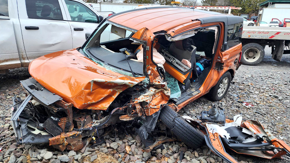 A small orange sport utility vehicle with its driver side door knocked off and front crumpled