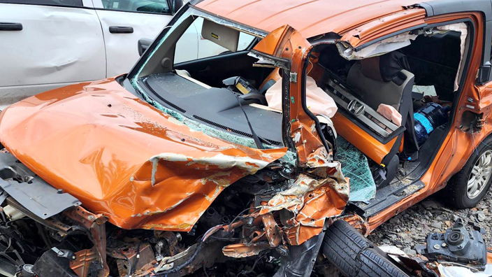 A small orange sport utility vehicle with its driver side door knocked off and front crumpled
