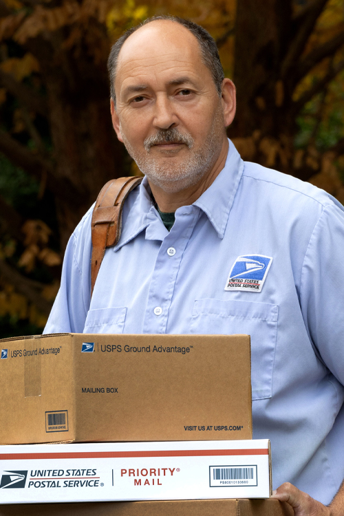 A uniformed USPS employee holding Priority Mail and USPS Ground Advantage
