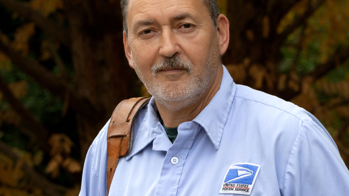 A uniformed USPS employee holding Priority Mail and USPS Ground Advantage