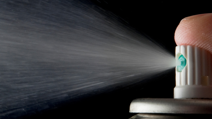 A finger presses down on the top of an aerosol can and releases spray.