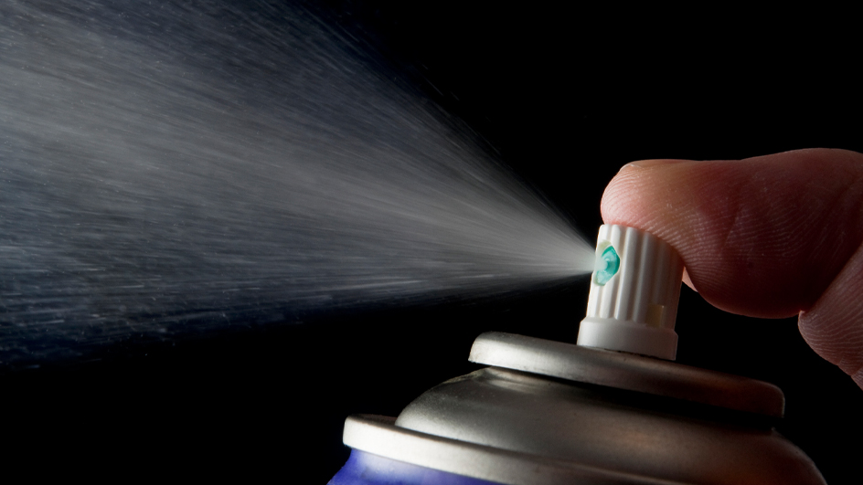 A finger presses down on the top of an aerosol can and releases spray.