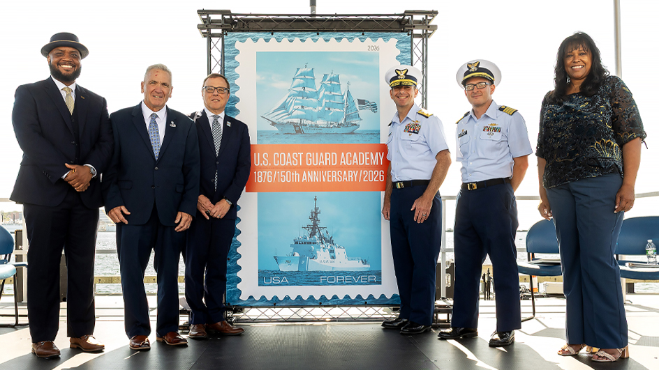 Six people standing on stage beside an enlarged image of the U.S. Coast Guard Academy stamp