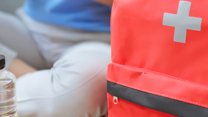 Closeup of an orange backpack and two bottles of water with a woman wearing a blue shirt in the background