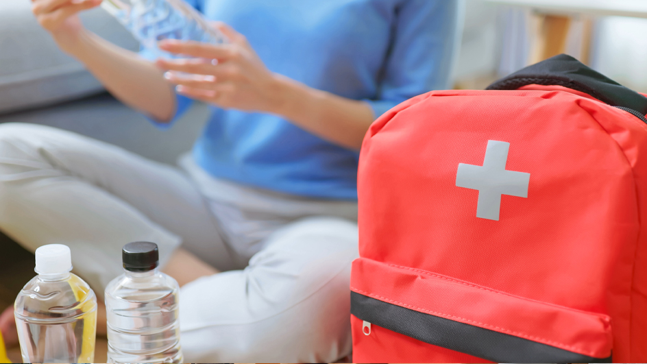 Closeup of an orange backpack and two bottles of water with a woman wearing a blue shirt in the background
