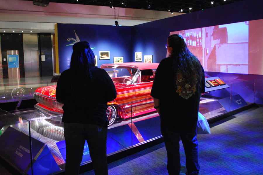 Two people looking at a red Chevrolet Impala in a dimly lit room