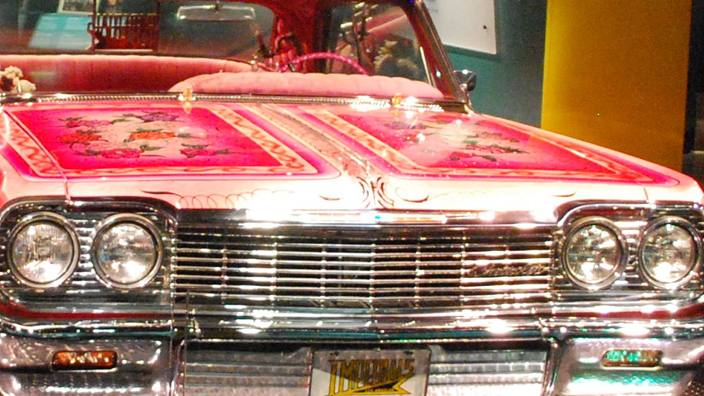 A red lowrider vehicle sitting on display in a dark room with a spotlight shining on it