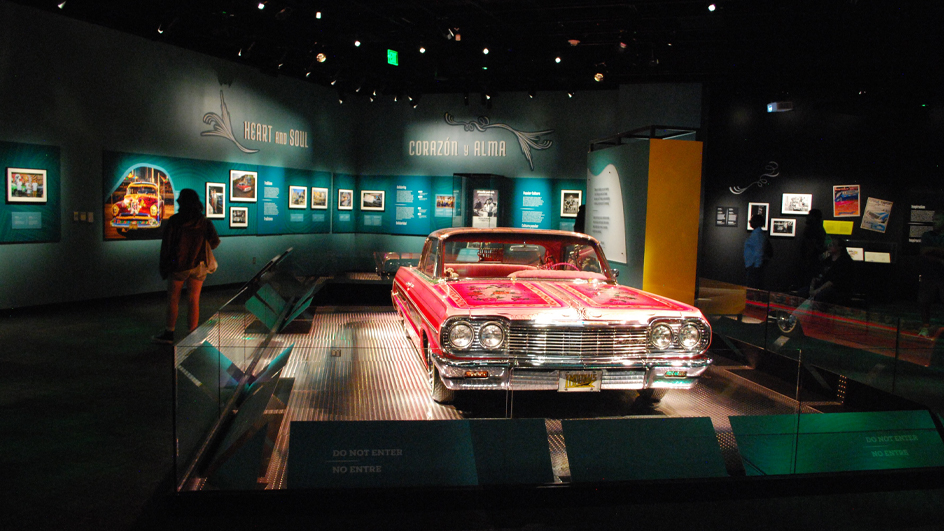 A red lowrider vehicle sitting on display in a dark room with a spotlight shining on it