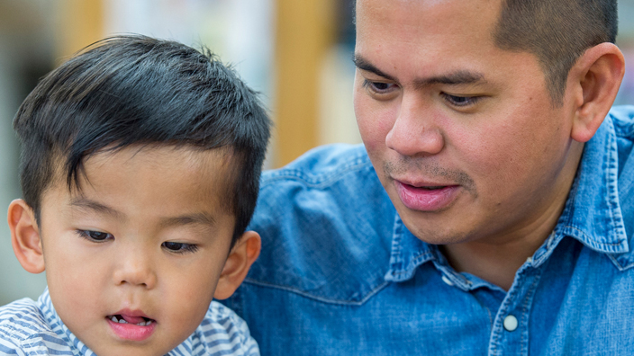 A father and young son in a library reading a book