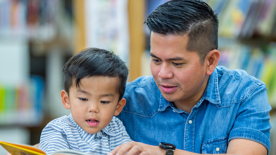A father and young son in a library reading a book