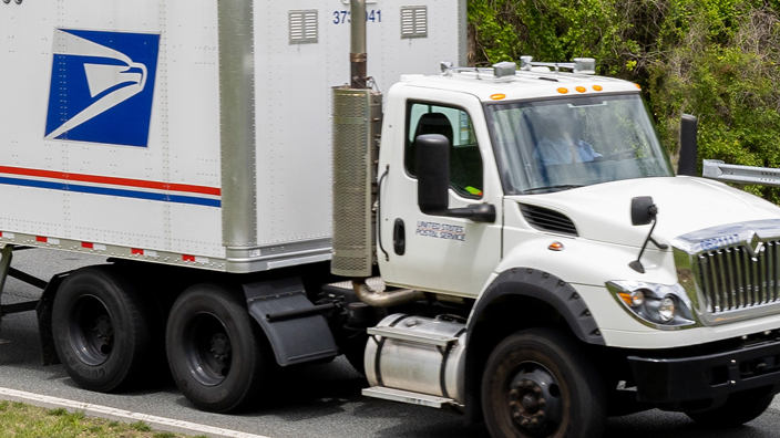 A Postal Service tractor trailer driving down a road