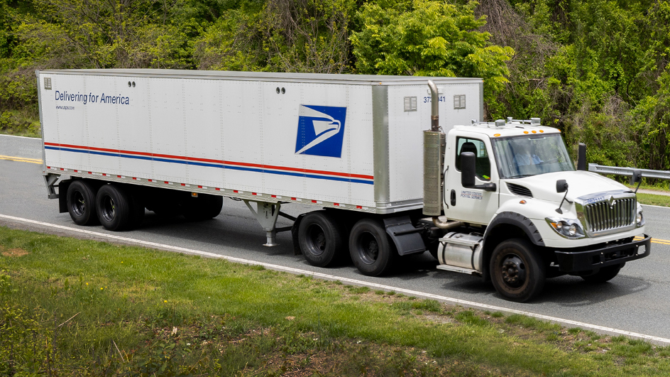 A Postal Service tractor trailer driving down a road