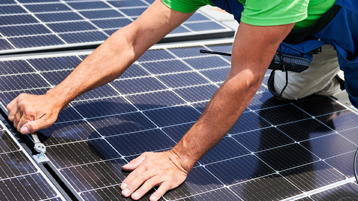 Close up of a man using a wrench to install solar panels on a roof