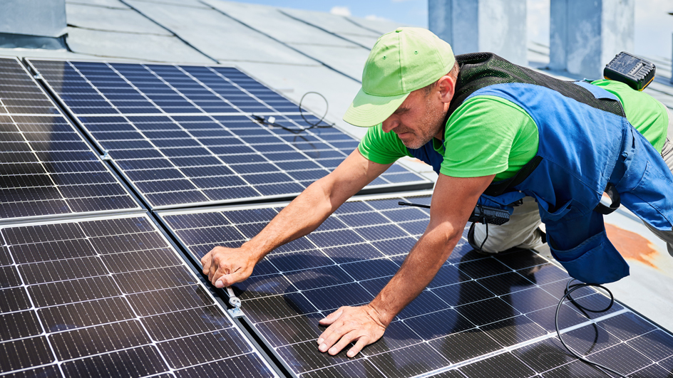 Close up of a man using a wrench to install solar panels on a roof