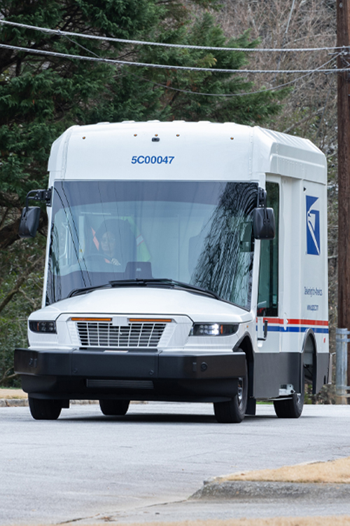 A USPS next-generation delivery vehicle driving down a residential street