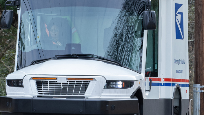 A USPS next-generation delivery vehicle driving down a residential street