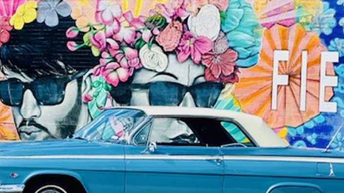 A blue lowrider vehicle parked in front of a colorful mural.