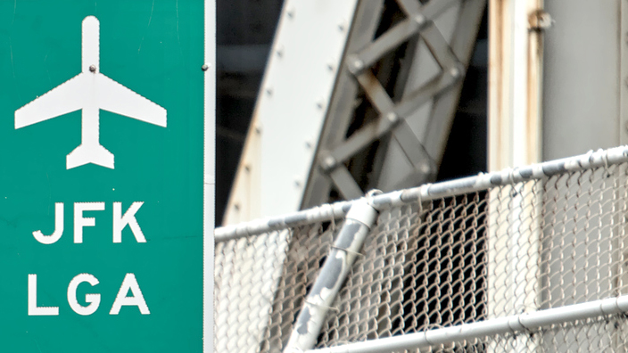 A green sign on a traffic light with Manhattan Bridge in the background