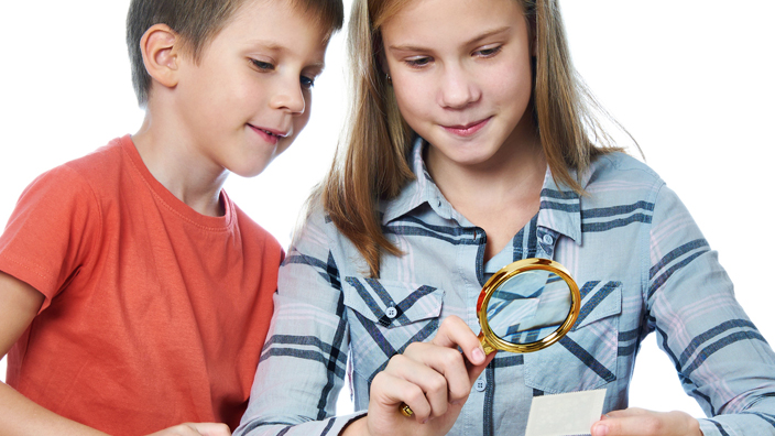 Teen girl and little boy with magnifying glass looking at a book of stamps
